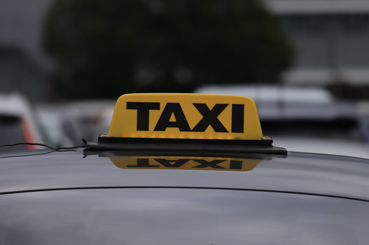 hero-img-02 Yellow taxi sign on a car roof in a city parking area during daylight.