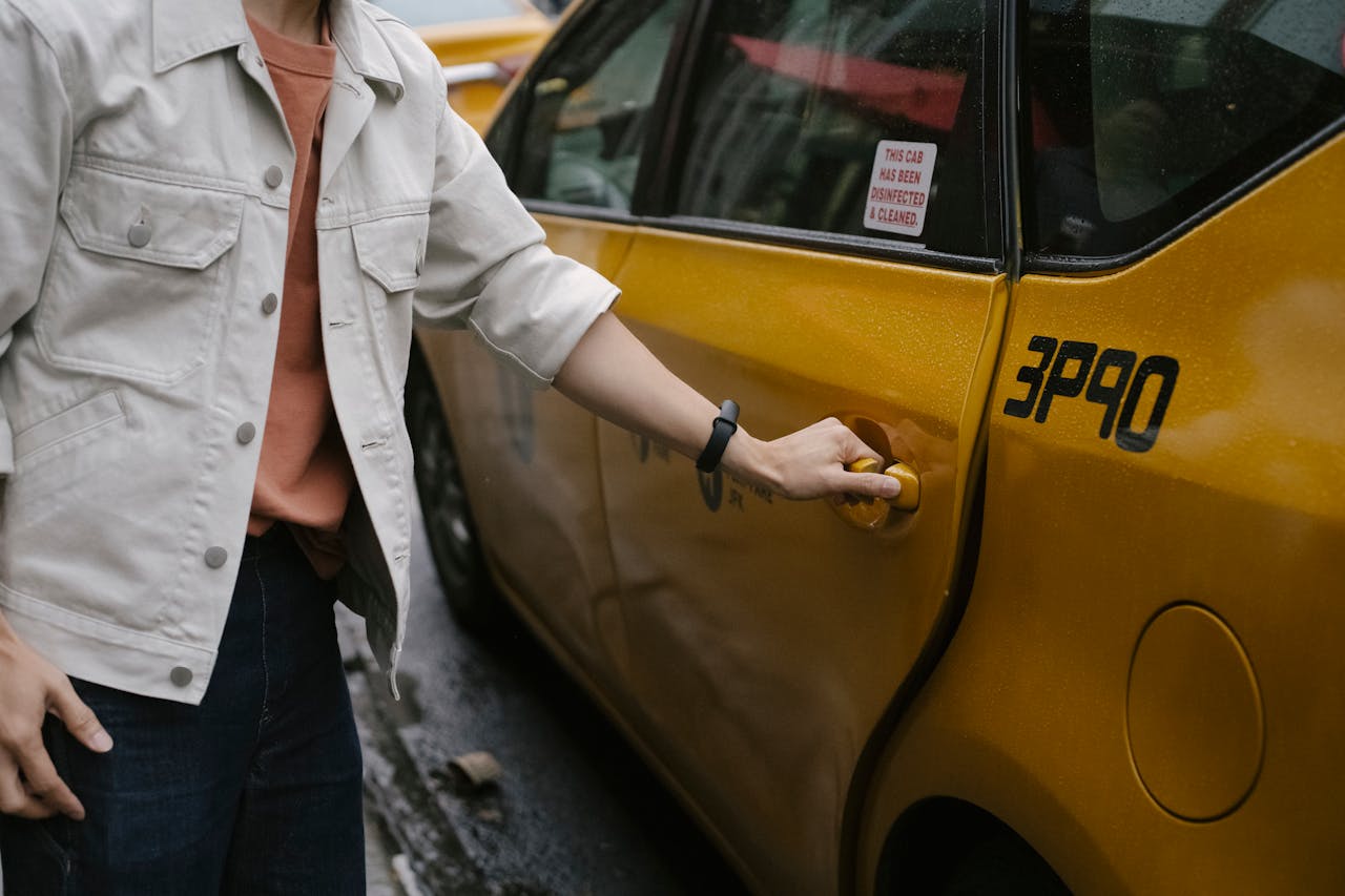 hero-img-01 Unrecognizable passenger in casual clothes opening door of cab parked on roadside in city on street while commuting to work